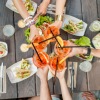 overhead view of friends toasting refreshments over a picnic table of food